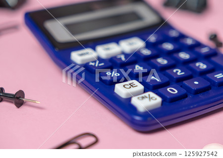 Blue calculator with focus on percent button surrounded by office supplies on soft pink background Blue calculator with focus on percent button surrounded by office supplies on soft pink background 125927542
