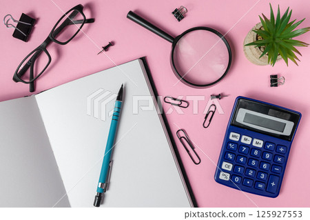 Notebook with pen, calculator, magnifying glass, glasses, plant and stationery on pink background 125927553
