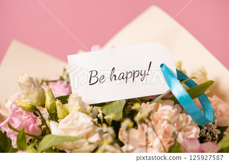 beautiful bouquet of pastel flowers with a handwritten be happy message card tied with a blue ribbon, spreading joy, positivity, and warm wishes on a soft pink background 125927587