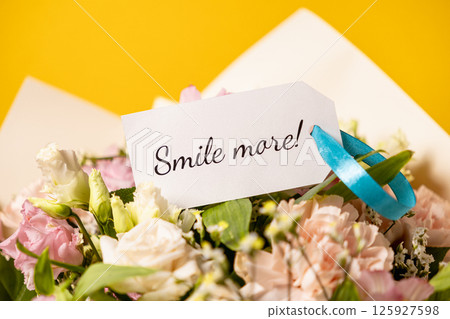 uplifting floral bouquet with heartfelt smile more message on elegant gift tag, accented by a delicate blue ribbon, set against a vibrant yellow background for a cheerful and inspiring touch 125927598