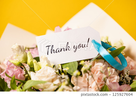 elegant floral bouquet with thank you message on gift tag, tied with blue ribbon, on yellow background elegant floral bouquet with thank you message on gift tag, tied with blue ribbon, on yellow background 125927604