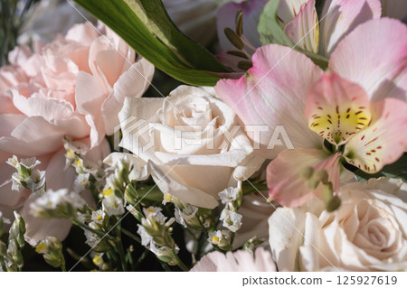 Delicate white and pink flowers in soft sunlight showcasing roses, carnations, and alstroemeria 125927619