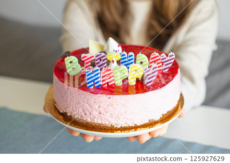 Colorful birthday cake with striped letter candles held by woman at festive indoor celebration Colorful birthday cake with striped letter candles held by woman at festive indoor celebration 125927629