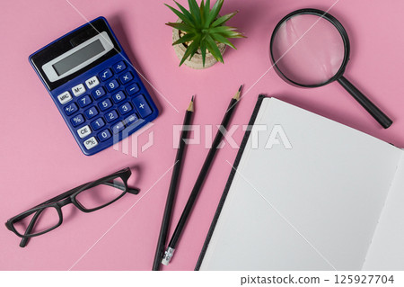 Blank notebook with calculator, glasses, office items flat lay on pink background symbolizes study and planning 125927704