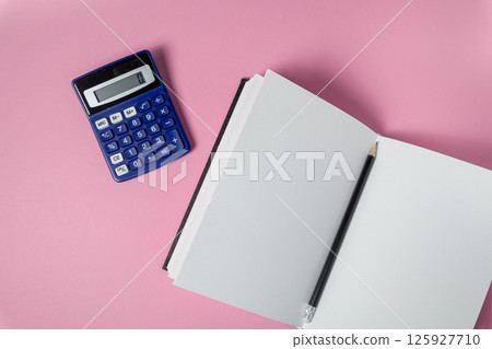 Blue calculator, blank notebook, pencil represent finance, education, strategy on pink background Blue calculator, blank notebook, pencil represent finance, education, strategy on pink background 125927710