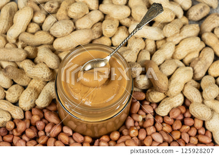 Peanut butter in a jar among scattered peanuts 125928207