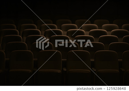 Dark empty cinema hall with soft ambient light over rows of theater seats creating moody cinematic atmosphere before film screening or movie premiere starts 125928648