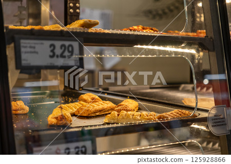Delicious freshly baked flaky pastries are displayed in a heated store bakery case, available for quick grab-and-go purchase as a convenient snack or treat option 125928866