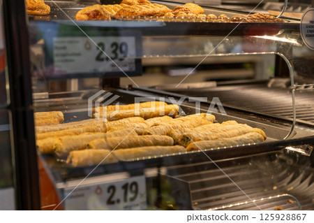 Delicious savory baked pastry rolls are displayed hot and ready in a heated store bakery case for convenient grab-and-go purchase as quick snack or meal options 125928867