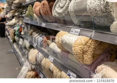 Shelves filled with rolled-up textiles like blankets and throws in various colors and textures, showcasing available home decor items during retail shopping Shelves filled with rolled-up textiles like blankets and throws in various colors and textures, showcasing available home decor items during retail shopping 125928870