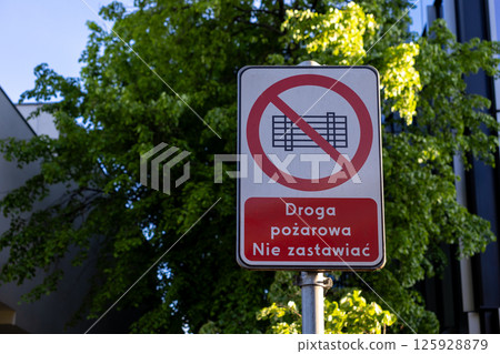 Regulatory sign with symbol and text Fire road Do not block (Droga pozarowa Nie zastawiac) on pole in urban setting ensuring emergency access 125928879