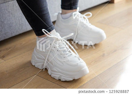 White chunky sole sneakers with laces and worn appearance on wooden floor, illustrating casual everyday footwear fashion and comfortable personal style 125928887