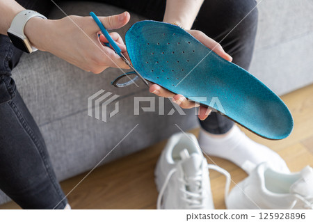 Close up of hands cutting blue insole with scissors indoors, customizing training footwear for enhanced athletic support Close up of hands cutting blue insole with scissors indoors, customizing training footwear for enhanced athletic support 125928896