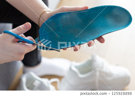 Person's hands using blue scissors to cut blue insole indoors, tailoring sport footwear for personalized comfort Person's hands using blue scissors to cut blue insole indoors, tailoring sport footwear for personalized comfort 125928898