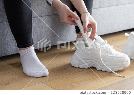 Close up of hands placing white shoe shaper into chunky athletic sneakers indoors, preserving shape for comfortable sport activity Close up of hands placing white shoe shaper into chunky athletic sneakers indoors, preserving shape for comfortable sport activity 125928900