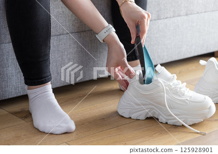 Close up of hands inserting blue insole into athletic training sneakers indoors, providing enhanced support for sport activity 125928901