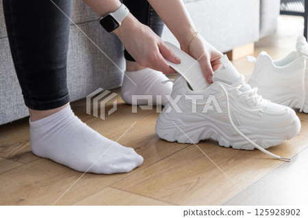 Hands inserting white shoe tree into chunky training sneakers indoors, maintaining footwear shape for active lifestyle Hands inserting white shoe tree into chunky training sneakers indoors, maintaining footwear shape for active lifestyle 125928902