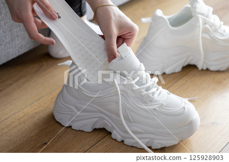 Close up of hands inserting white insole into chunky athletic sneakers indoors, providing customizable comfort for sport Close up of hands inserting white insole into chunky athletic sneakers indoors, providing customizable comfort for sport 125928903