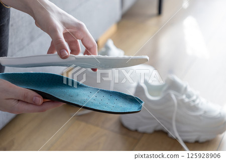 Close up of hands comparing blue and white insoles indoors, representing options for comfortable and supportive sport footwear 125928906