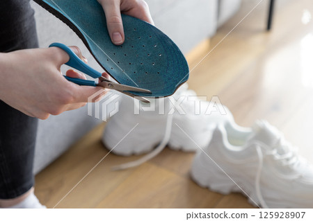 Close up of hands using blue scissors to trim blue insole, customizing sport shoes for enhanced comfort and performance Close up of hands using blue scissors to trim blue insole, customizing sport shoes for enhanced comfort and performance 125928907