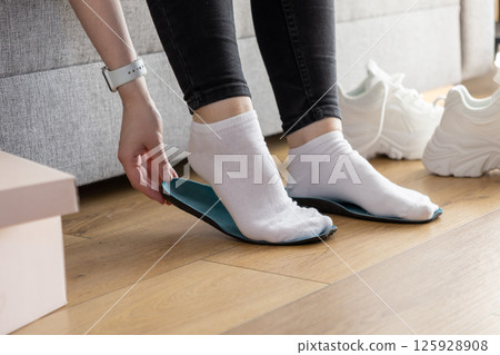 Person's hands placing blue insole onto socked foot indoors, preparing for comfortable and supportive athletic footwear wear 125928908