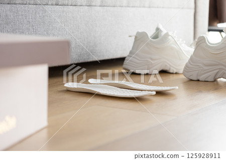 Pair of white athletic shoe insoles on wooden floor, representing comfort and support options for sport footwear customization Pair of white athletic shoe insoles on wooden floor, representing comfort and support options for sport footwear customization 125928911