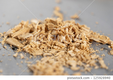 wood shavings scattered on a smooth gray surface, detailed close-up of rough wooden texture with small chips and splinters 125928940