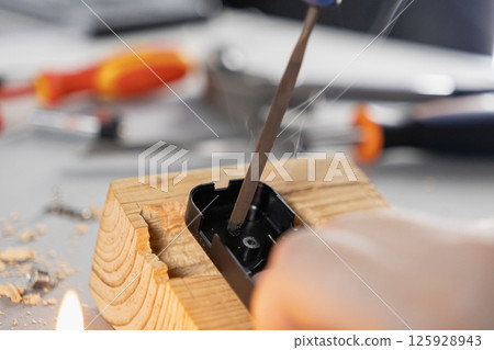 a person using a heated metal tool to make precise modifications to a small black object during a diy home repair project, with various tools in the background 125928943
