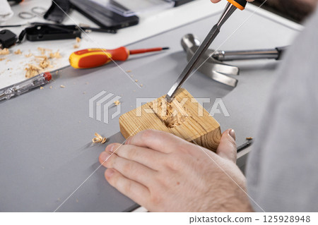 wood carving process with a sharp chisel on a wooden block, detailed diy woodworking project in a home workshop 125928948