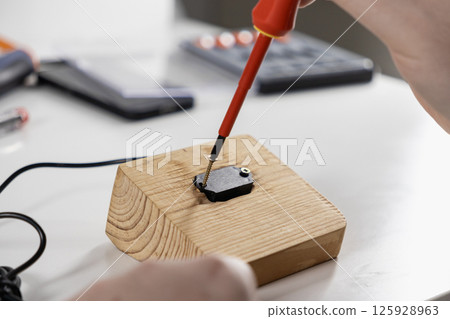 man using a screwdriver to secure an electronic component onto a wooden block during a diy assembly project man using a screwdriver to secure an electronic component onto a wooden block during a diy assembly project 125928963