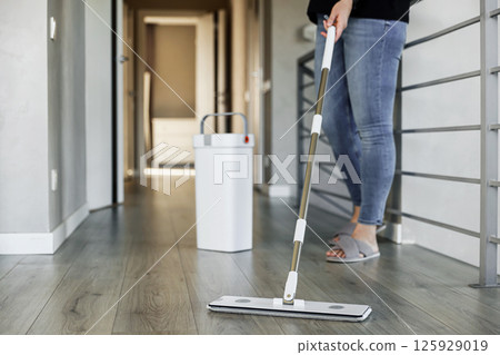 Woman mopping, wiping sleek hardwood floor in modern home setting. Housewife uses mop, bucket. Housekeeping, housework concept. Copy space. Sanitation, cleanliness, hygiene, cleanup, maintenance Woman mopping, wiping sleek hardwood floor in modern home setting. Housewife uses mop, bucket. Housekeeping, housework concept. Copy space. Sanitation, cleanliness, hygiene, cleanup, maintenance 125929019