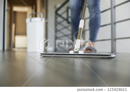 Woman mopping, wiping sleek hardwood floor in modern home setting. Housewife use cleaning mop in cozy living house room. Housekeeping, housework. Sanitation, cleanliness, hygiene, cleanup, maintenance 125929021