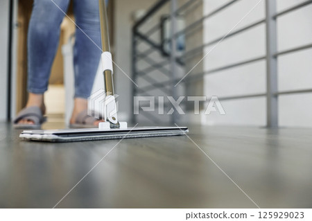 Woman mopping, wiping sleek hardwood floor in modern home setting. Housewife use cleaning mop in cozy living house room. Housekeeping, housework. Sanitation, cleanliness, hygiene, cleanup, maintenance Woman mopping, wiping sleek hardwood floor in modern home setting. Housewife use cleaning mop in cozy living house room. Housekeeping, housework. Sanitation, cleanliness, hygiene, cleanup, maintenance 125929023
