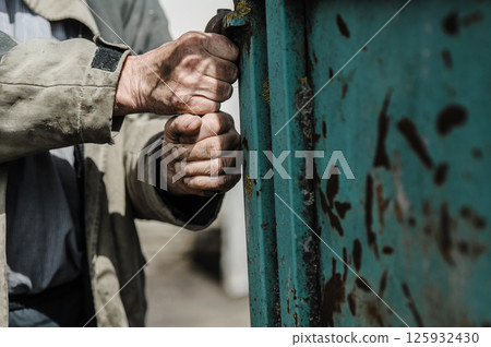 The worker's hands hold the rusty tool tightly, despite his fatigue. The worker's hands hold the rusty tool tightly, despite his fatigue. 125932430