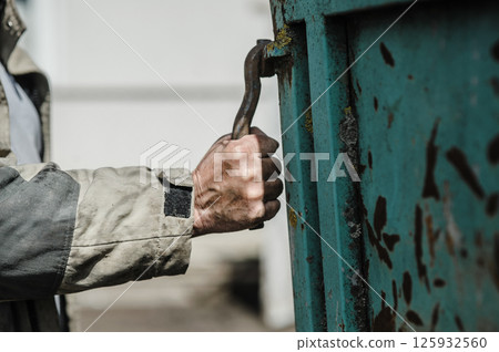 The worker's hands grip the latch of the trailer, which is rough and covered with dirt. The worker's hands grip the latch of the trailer, which is rough and covered with dirt. 125932560