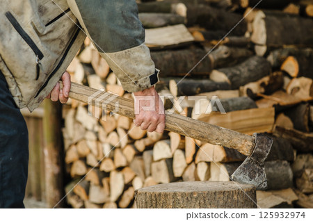 The old man's hand is clutching an axe stuck in a tree stump. 125932974