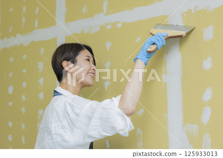 A woman applying putty to plasterboard 125933013
