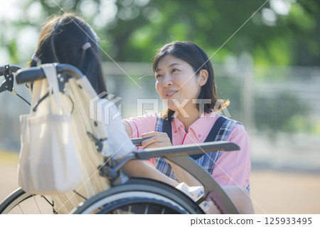 A caregiver pushing a wheelchair carrying an elementary school student 125933495