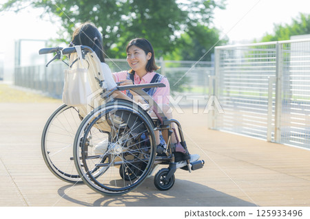 A caregiver pushing a wheelchair carrying an elementary school student A caregiver pushing a wheelchair carrying an elementary school student 125933496
