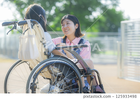 A caregiver pushing a wheelchair carrying an elementary school student A caregiver pushing a wheelchair carrying an elementary school student 125933498