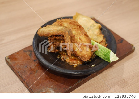 a serving of Indonesian fried chicken placed on a traditional black stone plate a serving of Indonesian fried chicken placed on a traditional black stone plate 125933746