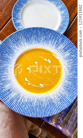 Tasty yellow cream soup in the restaurant on the beautiful blue plate. Tasty yellow cream soup in the restaurant on the beautiful blue plate. 125933982