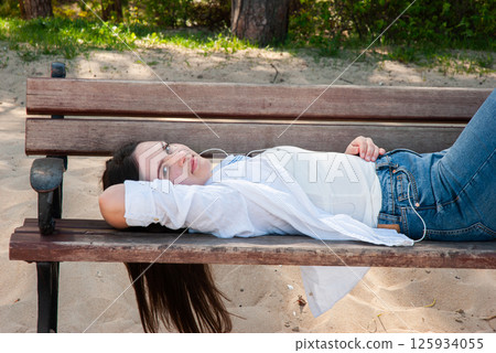 Young caucasian female in casual attire relaxing on a wooden bench at a sandy beach on a sunny day with nature in the background. Digital nomad lifestyle. Remote work 125934055