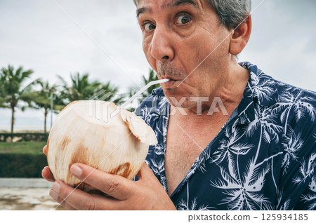 happy elderly male tourist drinks a drinking coconut with a straw on vacation on the beach by the sea in the tropics 125934185