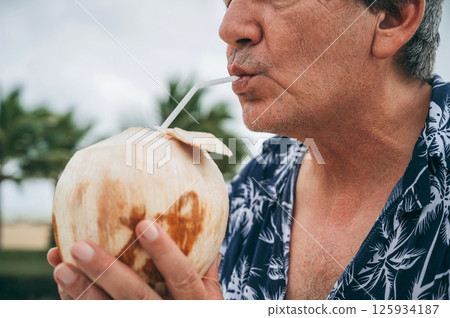 elderly male tourist drinks a drinking coconut through a straw on vacation at the beach elderly male tourist drinks a drinking coconut through a straw on vacation at the beach 125934187