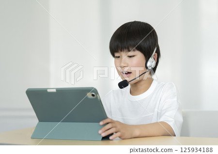 一名四年級男孩戴著耳機，面對著一台平板電腦 125934188