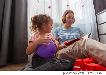 Bottom view of Caucasian young mother and little cute daughter are reading a book with fairy tales. Happy family spends time together. Concept of preschool education for children and Mother's Day 125934363