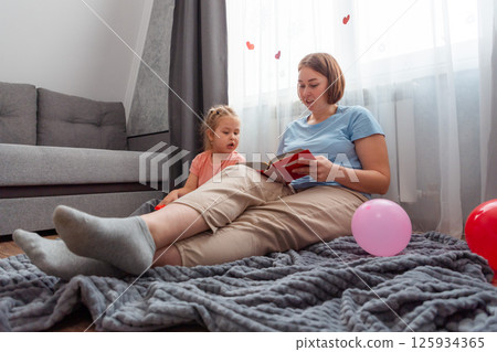 Bottom view of Caucasian young mother and little daughter are reading book with fairy tales. Concept of preschool education for children and Mother's Day Bottom view of Caucasian young mother and little daughter are reading book with fairy tales. Concept of preschool education for children and Mother's Day 125934365