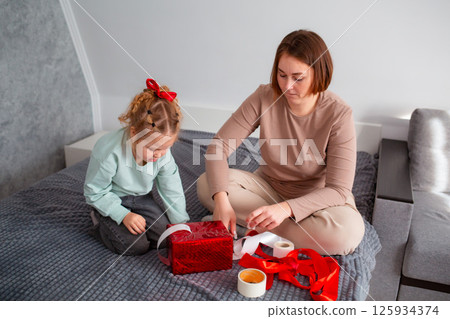 Top view of mother and daughter together packing a Valentine's Day and Mother's day gift. Caucasian woman and a little girl are preparing for the holiday Top view of mother and daughter together packing a Valentine's Day and Mother's day gift. Caucasian woman and a little girl are preparing for the holiday 125934374