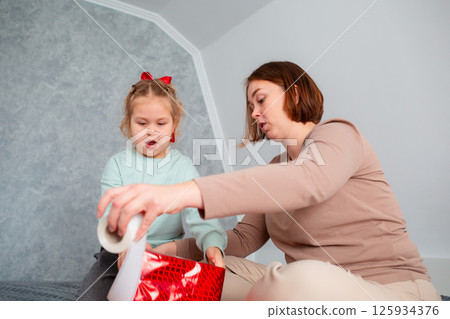 Bottom view of Caucasian mother and little cute daughter pack a holiday gift together. Woman teaches a child holiday preparation. Family celebration of Mother's Day 125934376